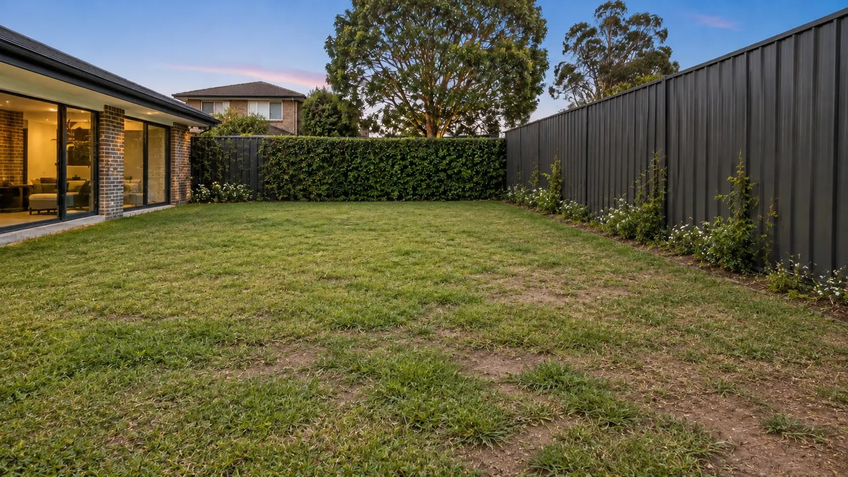 Before landscaping: patchy grass beside a dark fence